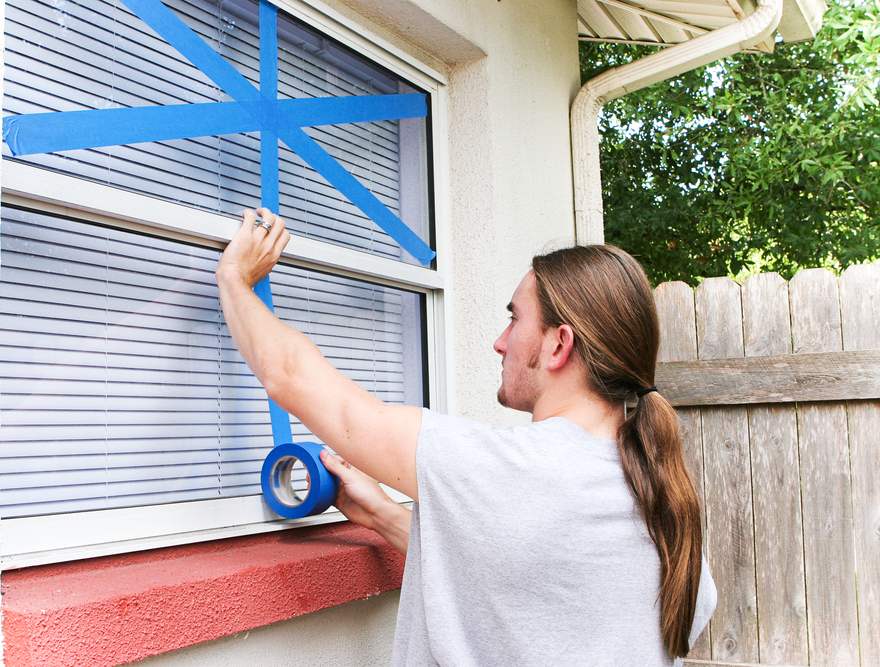 A man taping his windows with blue painters tape.